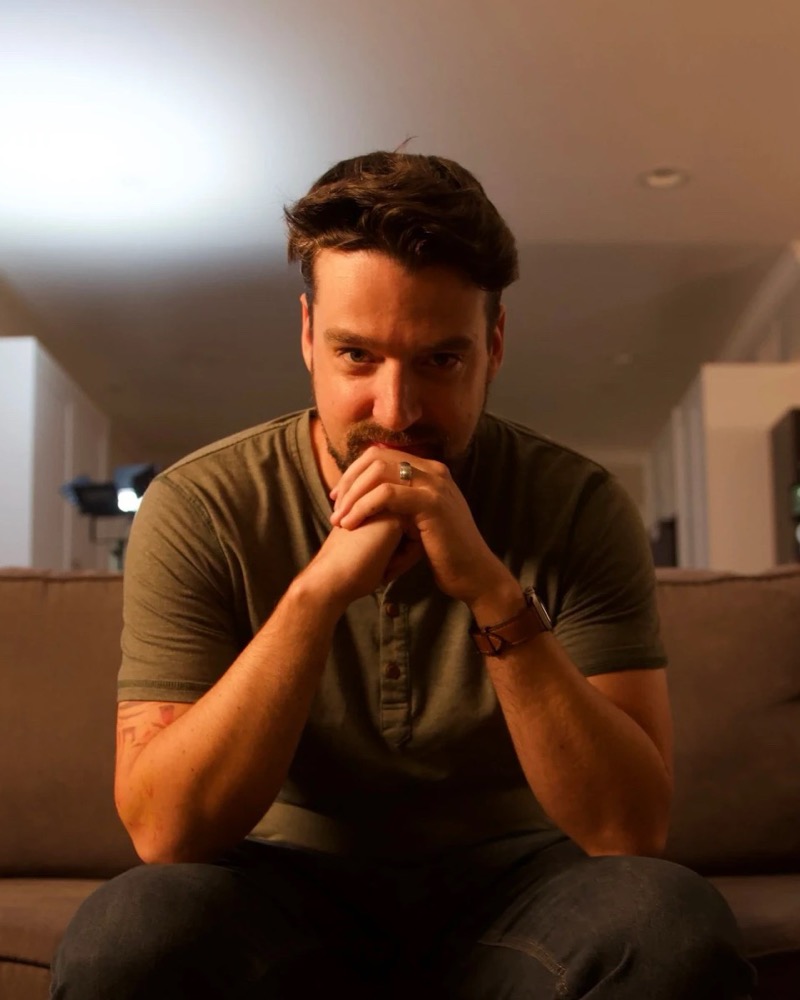 Justin Zagri, seated on a couch, hands clasped, looking at the camera